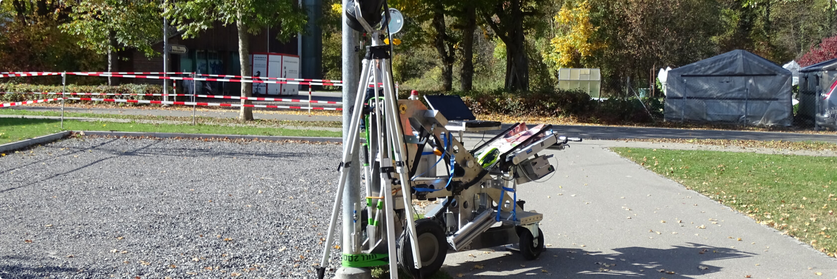 Auf einem Sportplatz wird bei Sonnenschein ein Mast mittels Mastbiegeverfahren geprüft.