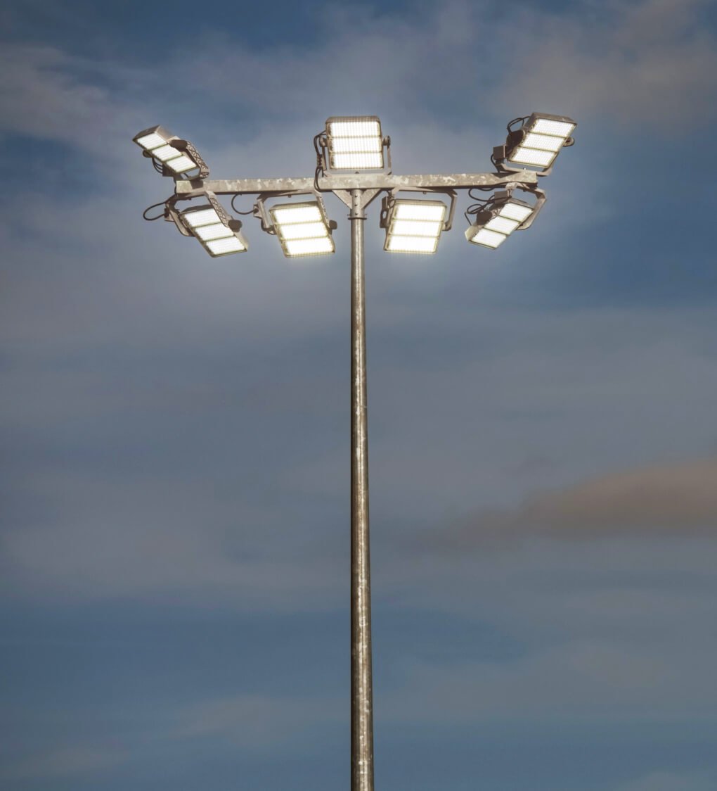 Eingeschaltete Flutlichtanlage auf einem Sportplatz bei eindunkelndem Himmel.