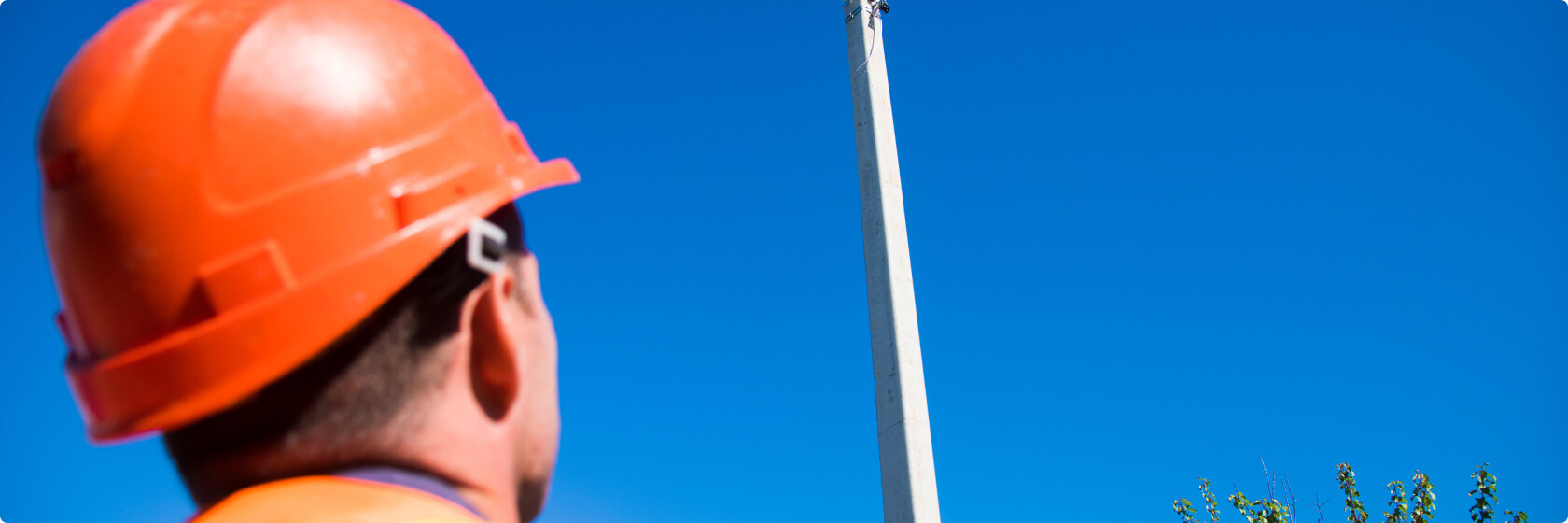 Un employé inspecte un mât d’éclairage sous un ciel bleu.